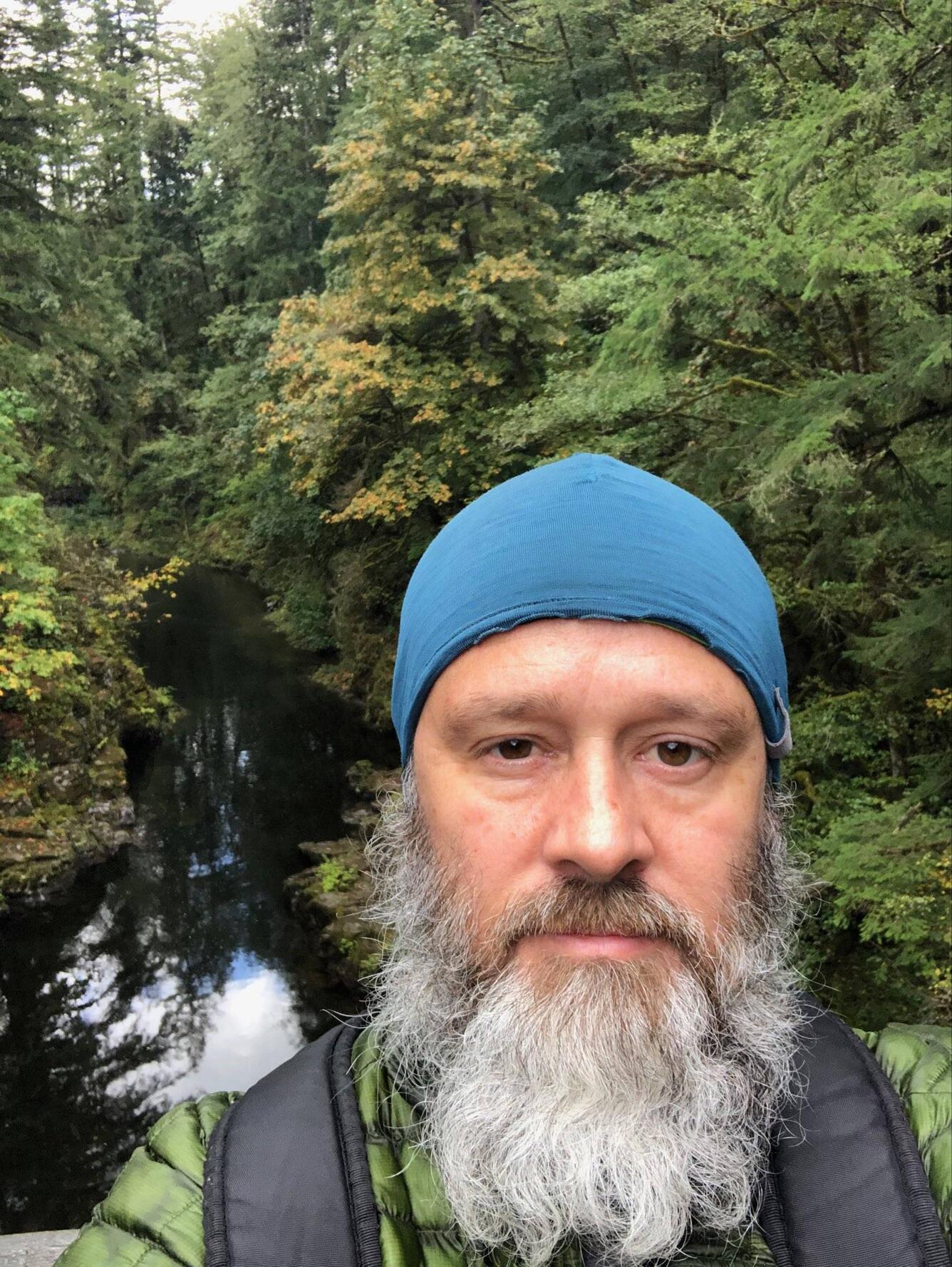 Man with beard and hat with woods and waterfall