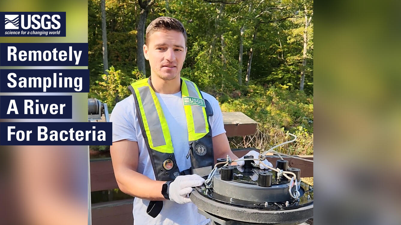 Wearing a personal flotation device, a scientist points to a bacteria sampler. Text: Remotely Sampling a River For Bacteria