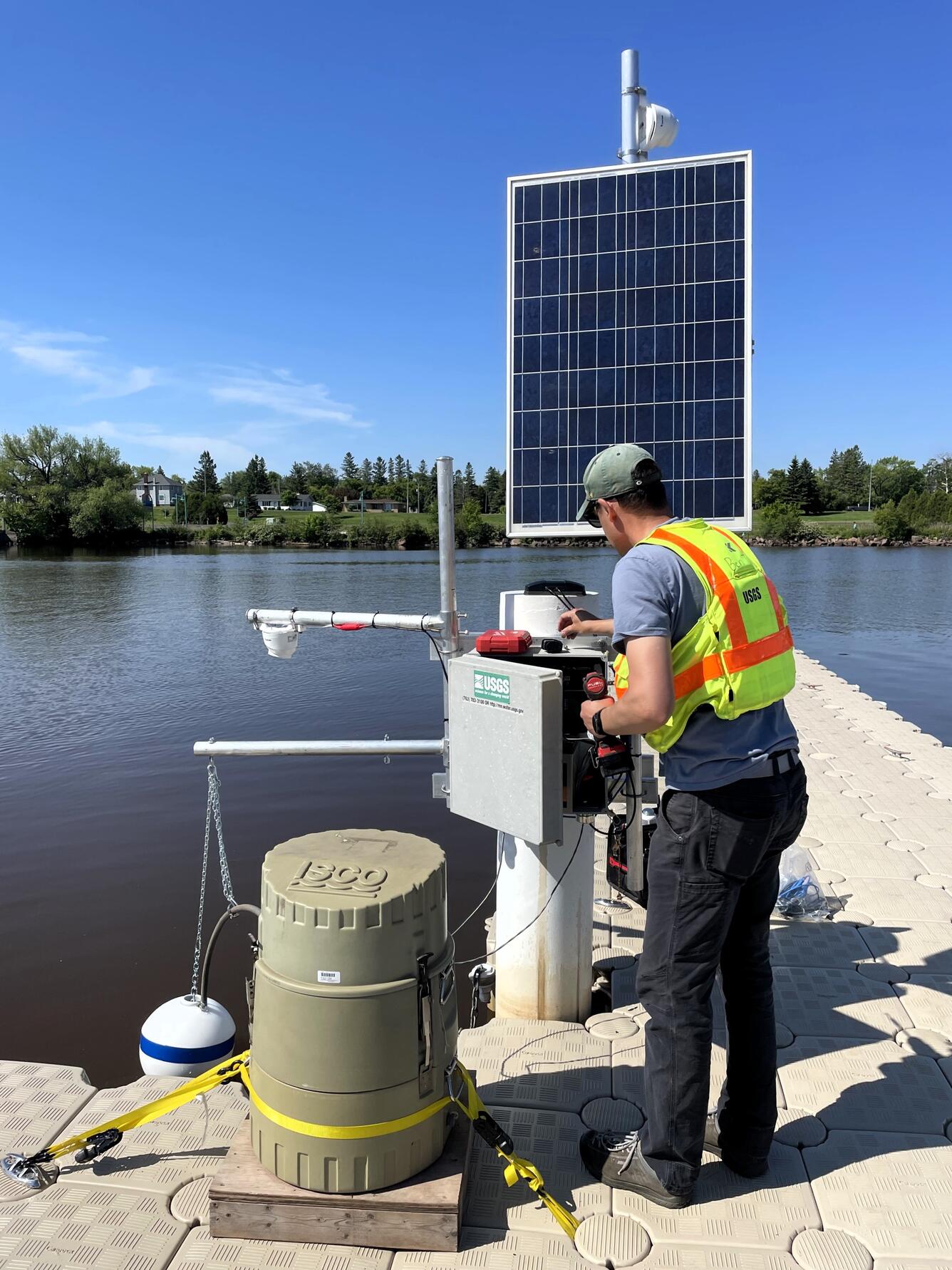 USGS hydrologic technician installs equipment inside streamgage housing on shore of lake