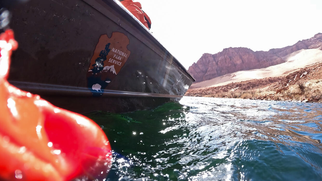 A close up of the National Park Service logo on a flat boat floating in a river.