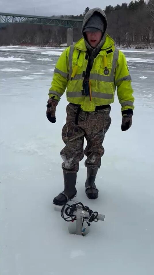 Scientist standing behind borehole in ice with an acoustic probe lowered