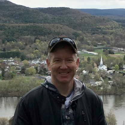 man with a hat standing in front of a town in the distance