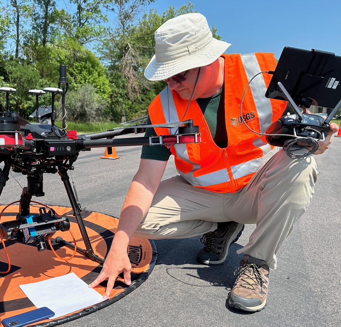 Matthew Burgess, kneeling before launchpad, prepares drone aircraft for flight