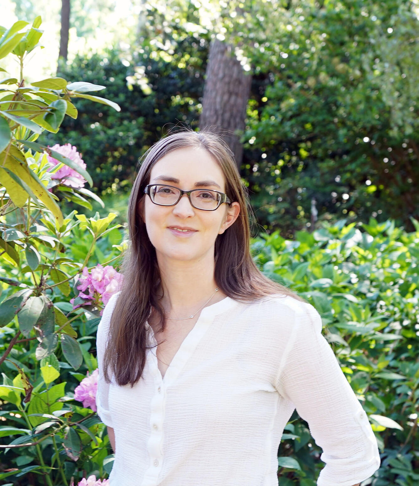 A white woman with long brown hair and glasses wearing a button-down shirt.