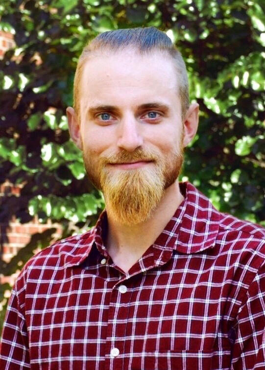 Blond man standing near a tree with a red and white plaid shirt