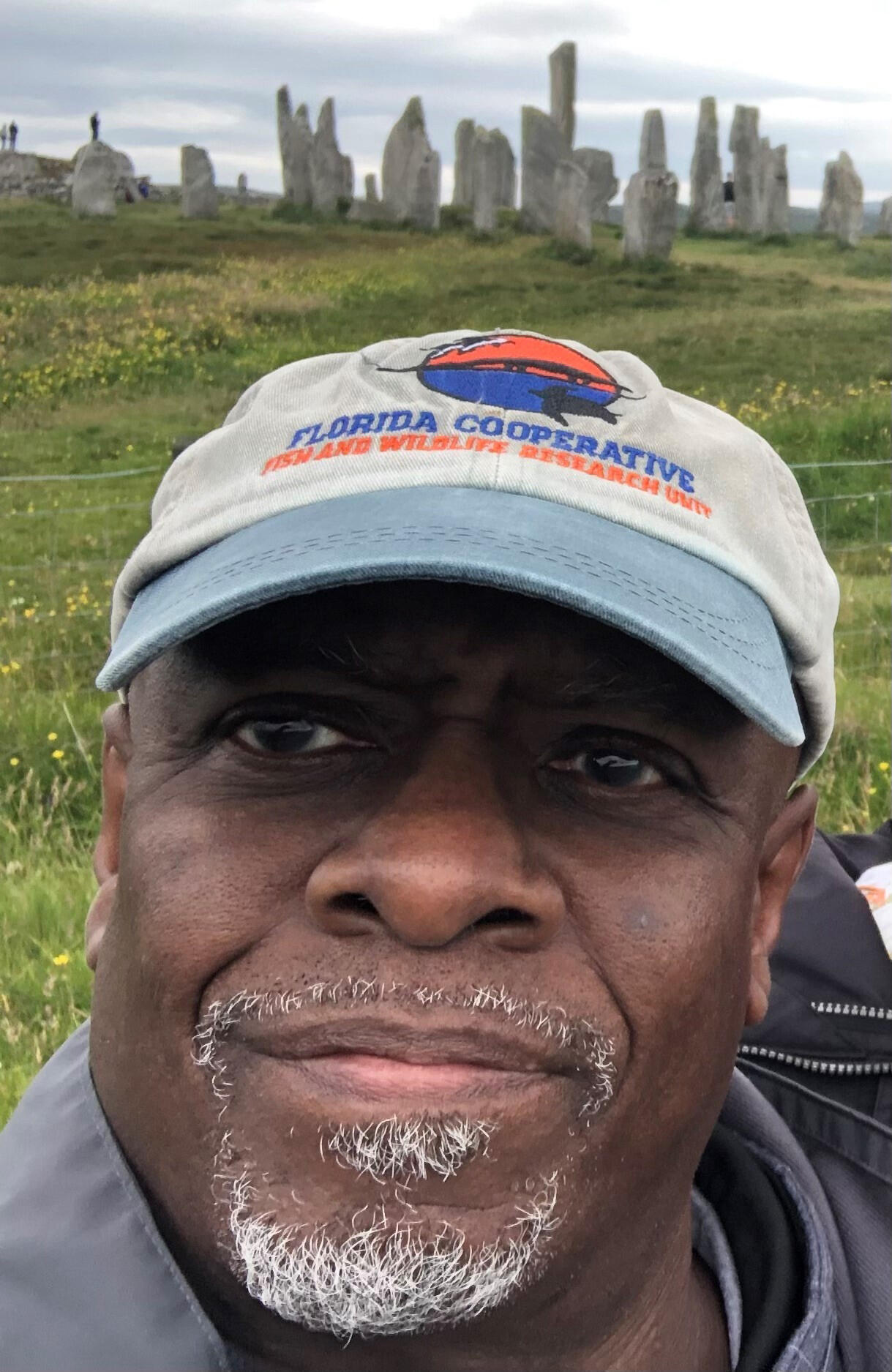 man wearing a hat standing near large rock outcroppings and green grass