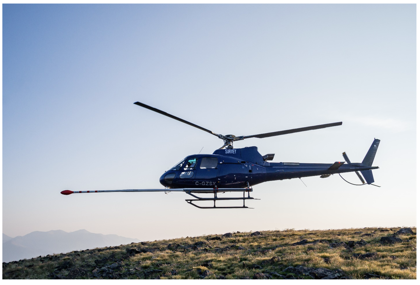 Blue helicopter with boom protruding in front, silhouetted in flight against the sky, rotors frozen in time.