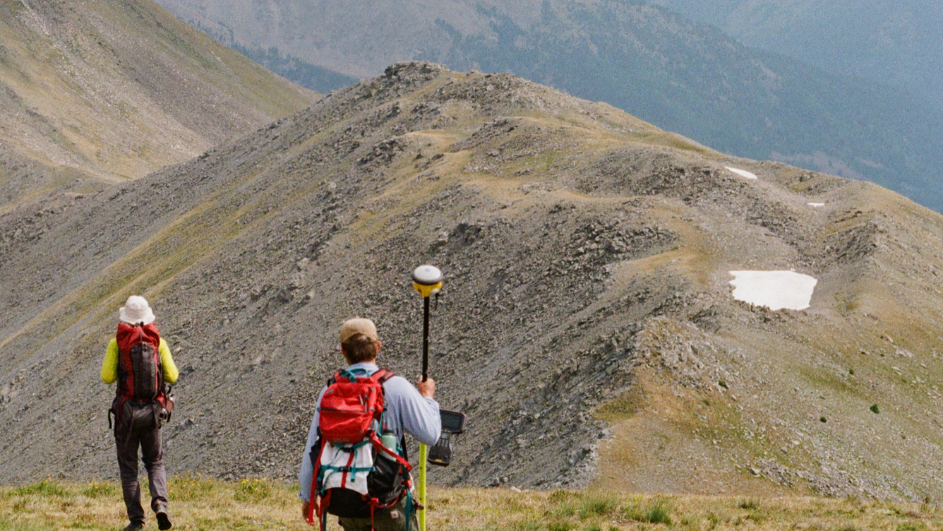 two people walking on hillslope holding equipment