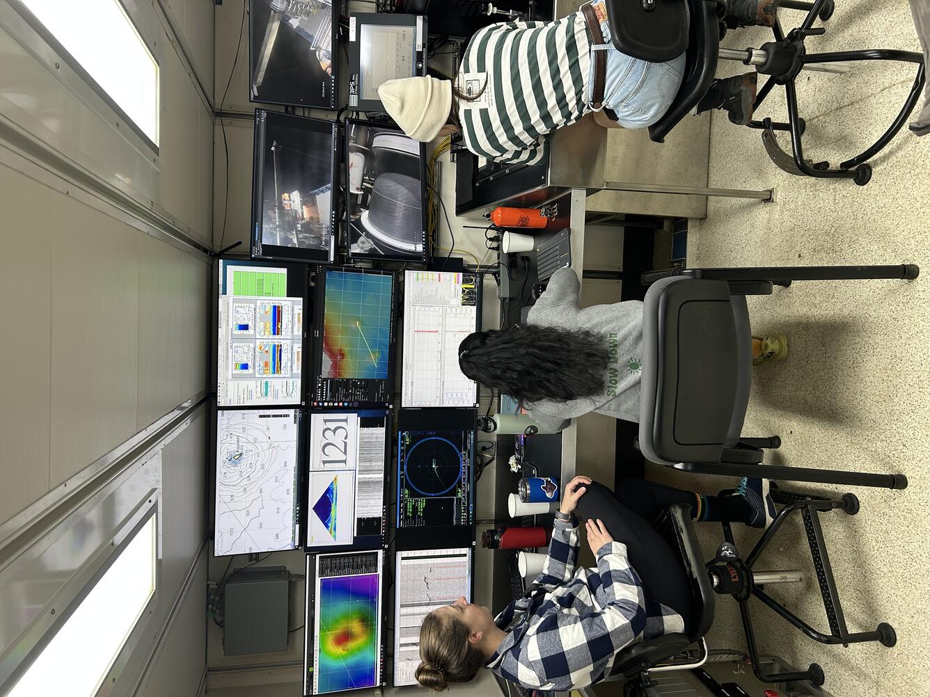 Three people sit in chairs facing multiple computer screens