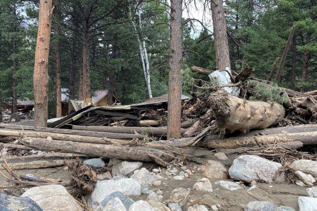 Damaged house surrounded by rocks, trees, and mud