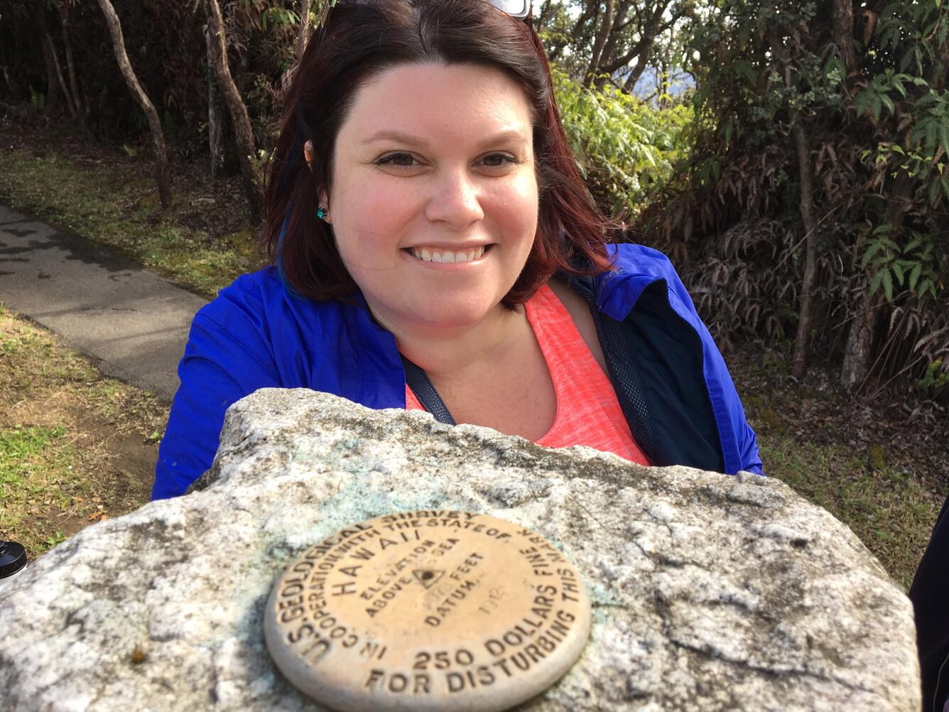 Woman standing behind USGS benchmark on rock in Hawaii