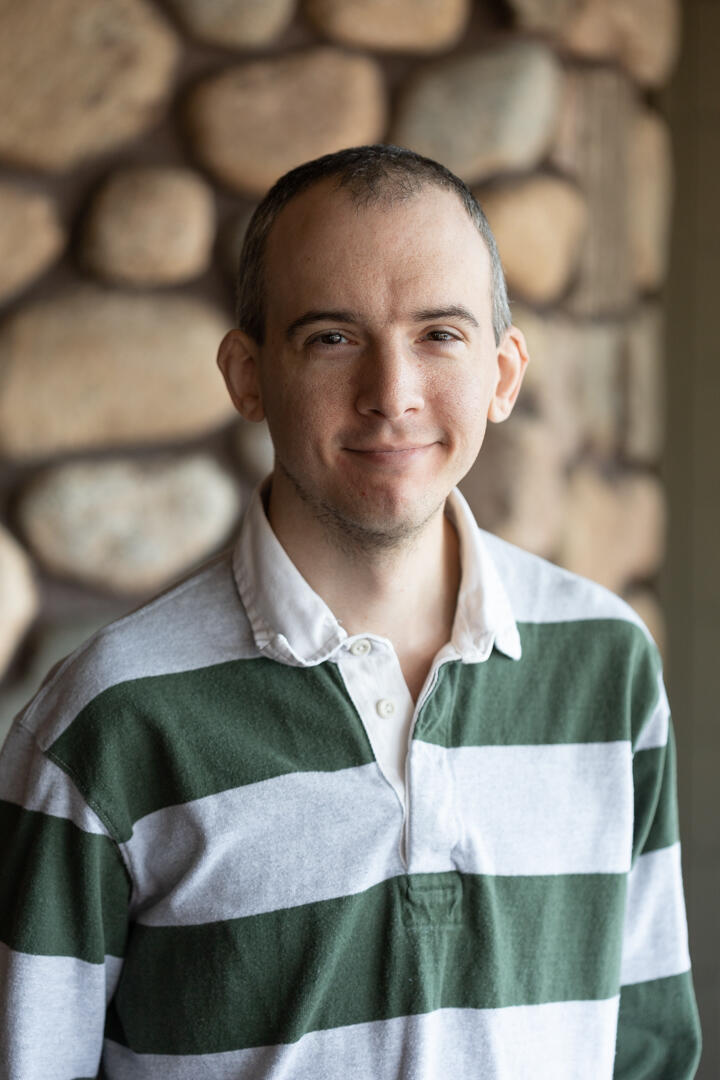 Man in green and gray striped collared shirt standing against stone backdrop