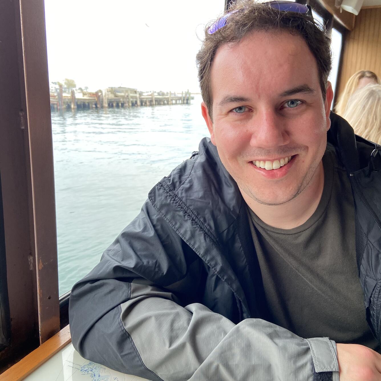 Smiling man leaning against table with lake in background.
