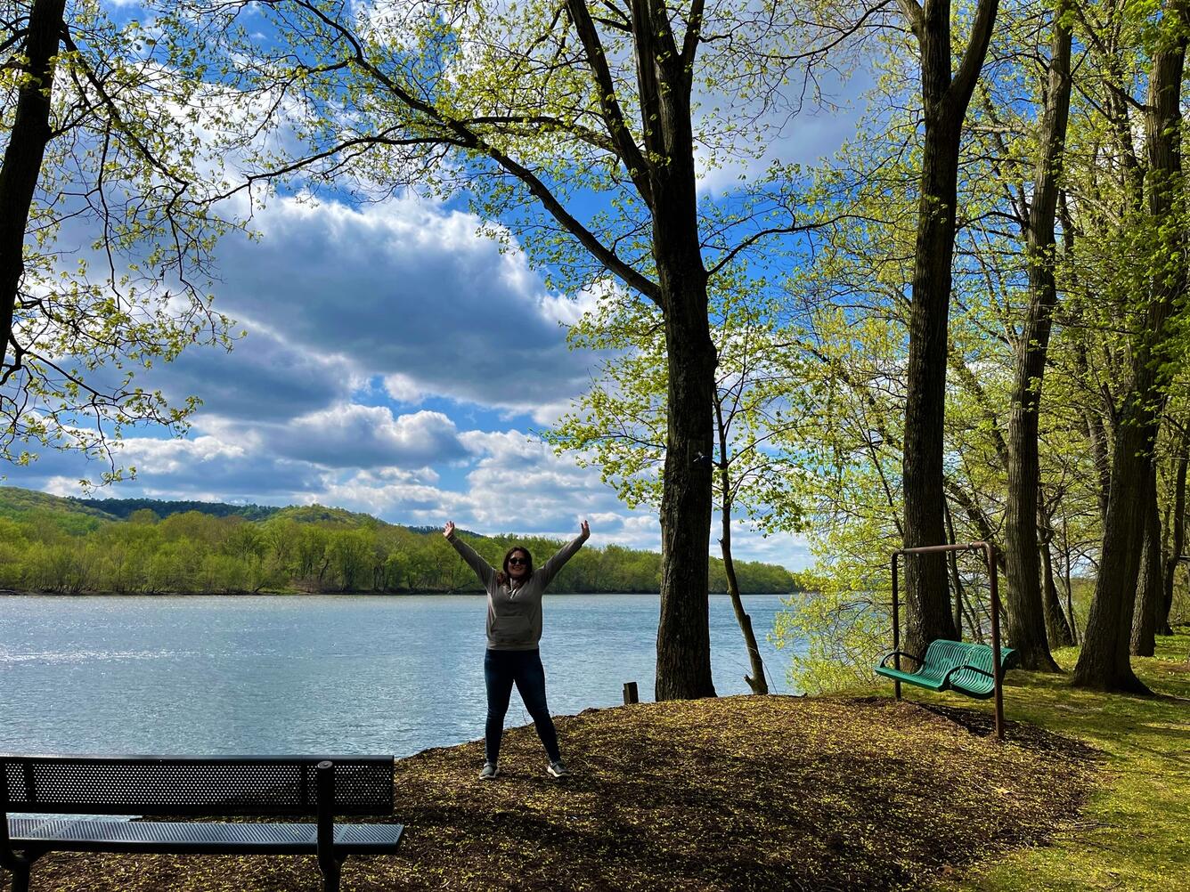 A PhD student is standing with her arms up in joy in front of the beautiful Susquehanna River highlighted by a blue sky scatt