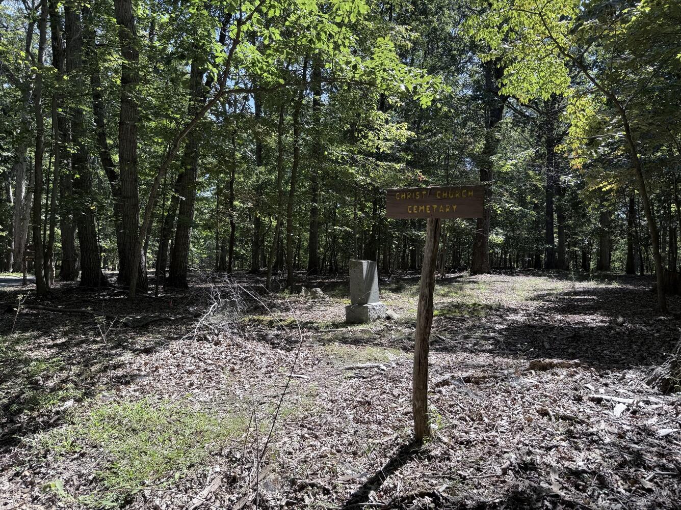 Wooded clearing with a small cemetery sign and one headstone.