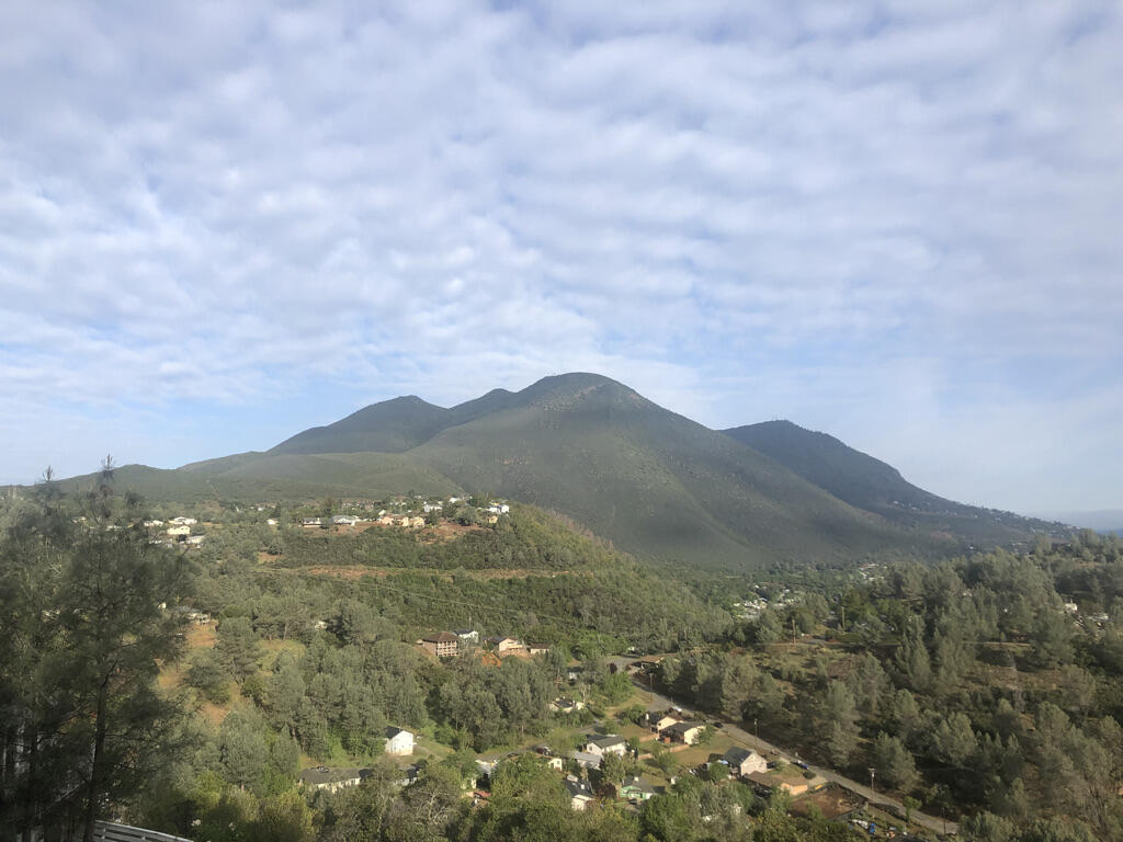In the distance, a five-peaked mountain covered in dark green trees rises above a series of lower hills