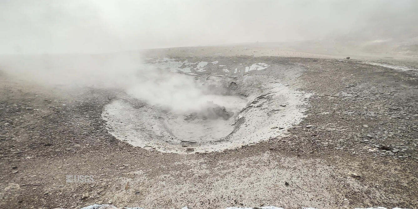 Small area of gray mud bubbling with steam 