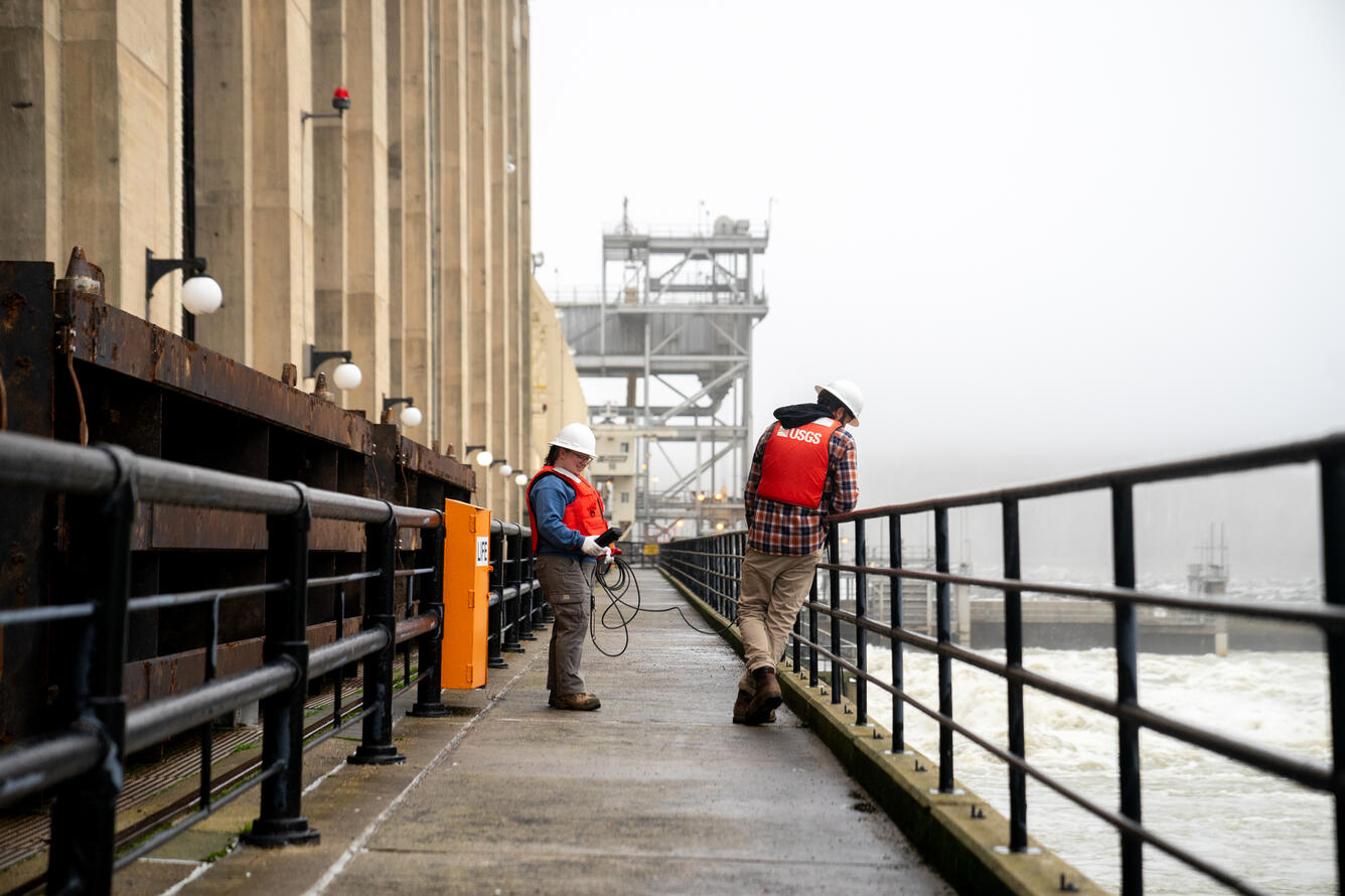 Kelly McVicker examines the sonde readings on the dam catwalk, as Shane Mizelle holds the sonde with a cable in the water below.