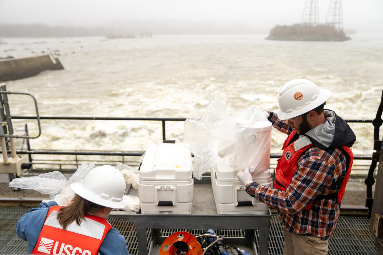 Standing on a catwalk, hydrologic technicians Kelly McVicker and Shane Mizelle prepare to collect water samples from the Conowingo Dam.