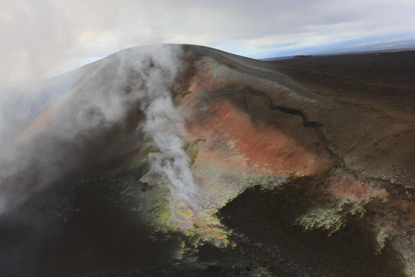 A brown hill of volcanic tephra with a crack and yellow and orange areas of alteration