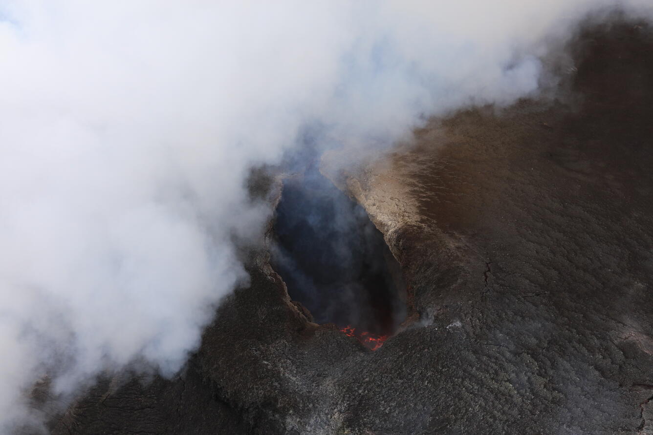 Close-up image of a volcanic vent with red lava surface far below the vent rim
