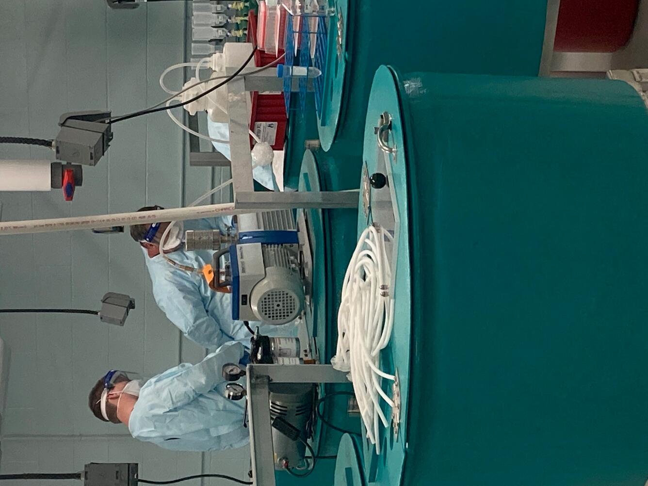 Two men in full protective gear work on samples in a lab.