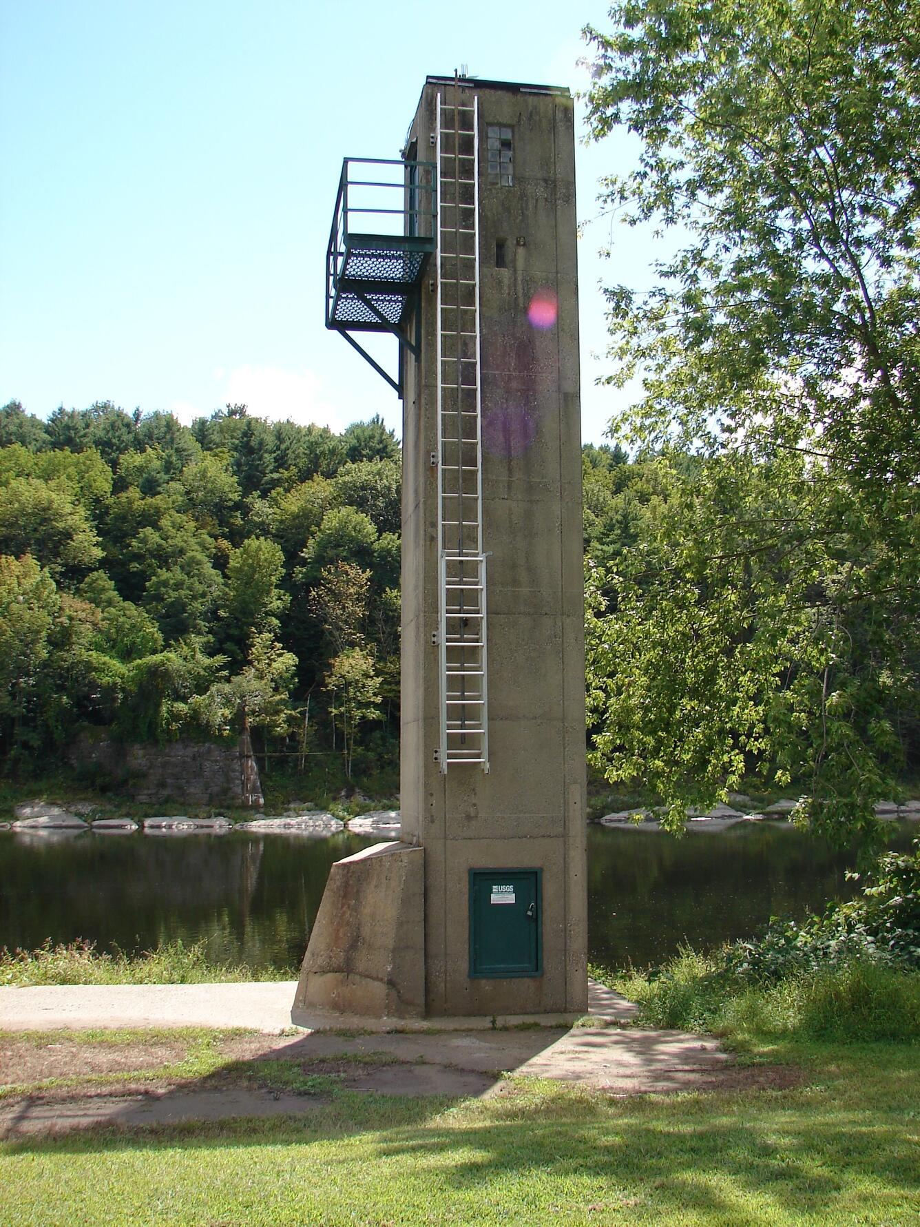 A four-story concrete tower stands next to the river, a ladder leading up to the landing platform