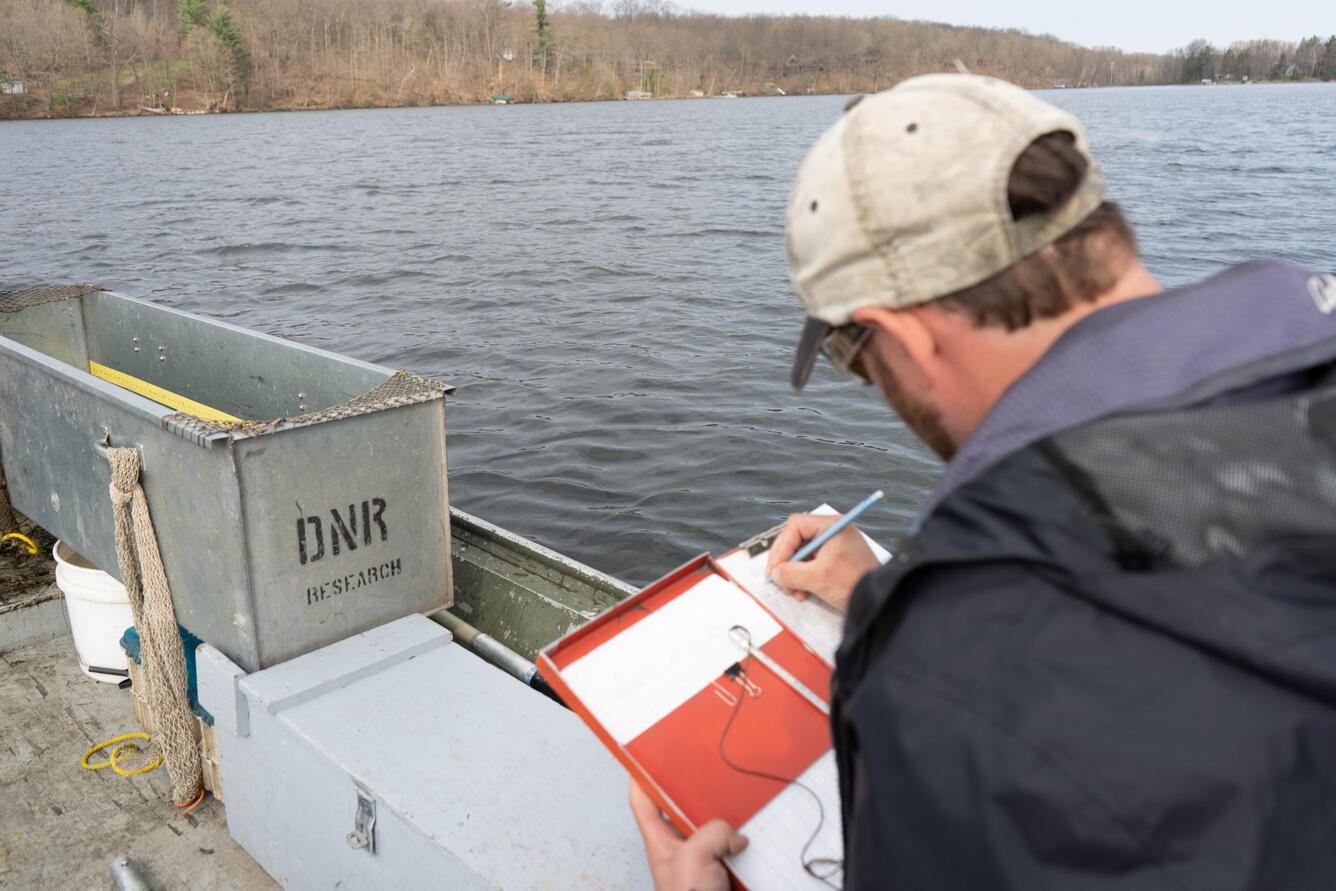 A person sits in a boat on a lake taking notes