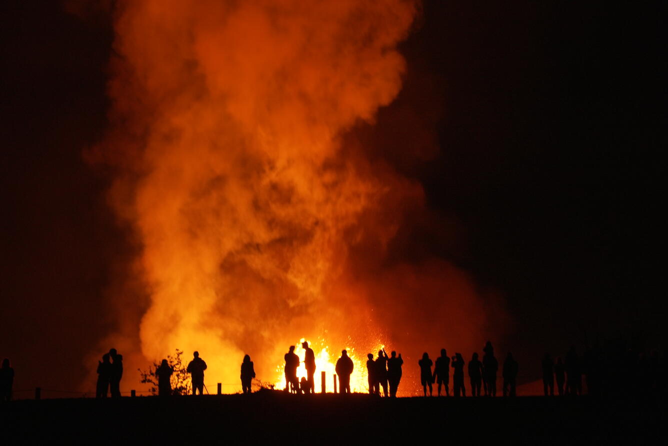 Silhouettes of people at night with a lava fountain and plume behind them