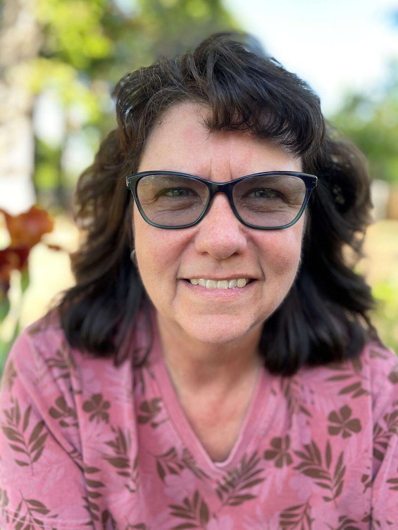 woman with brown hair and glasses wearing a pink sweater