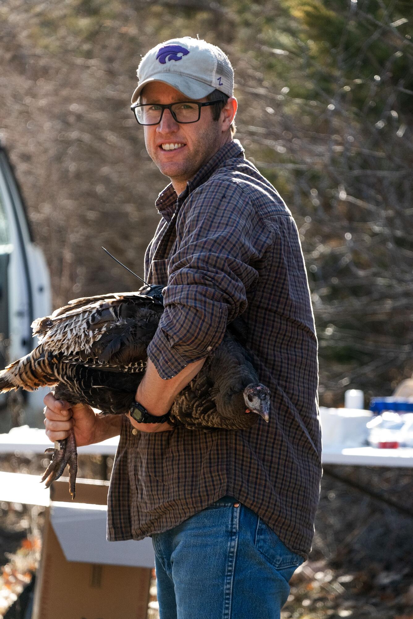 scientist wearing a hat, blue shirt, is holding a wild turkey