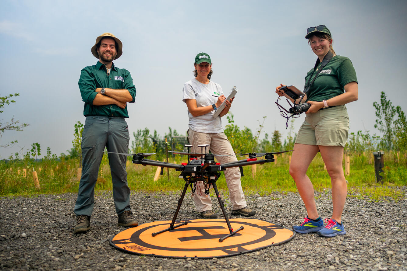 Three people standing behind a drone