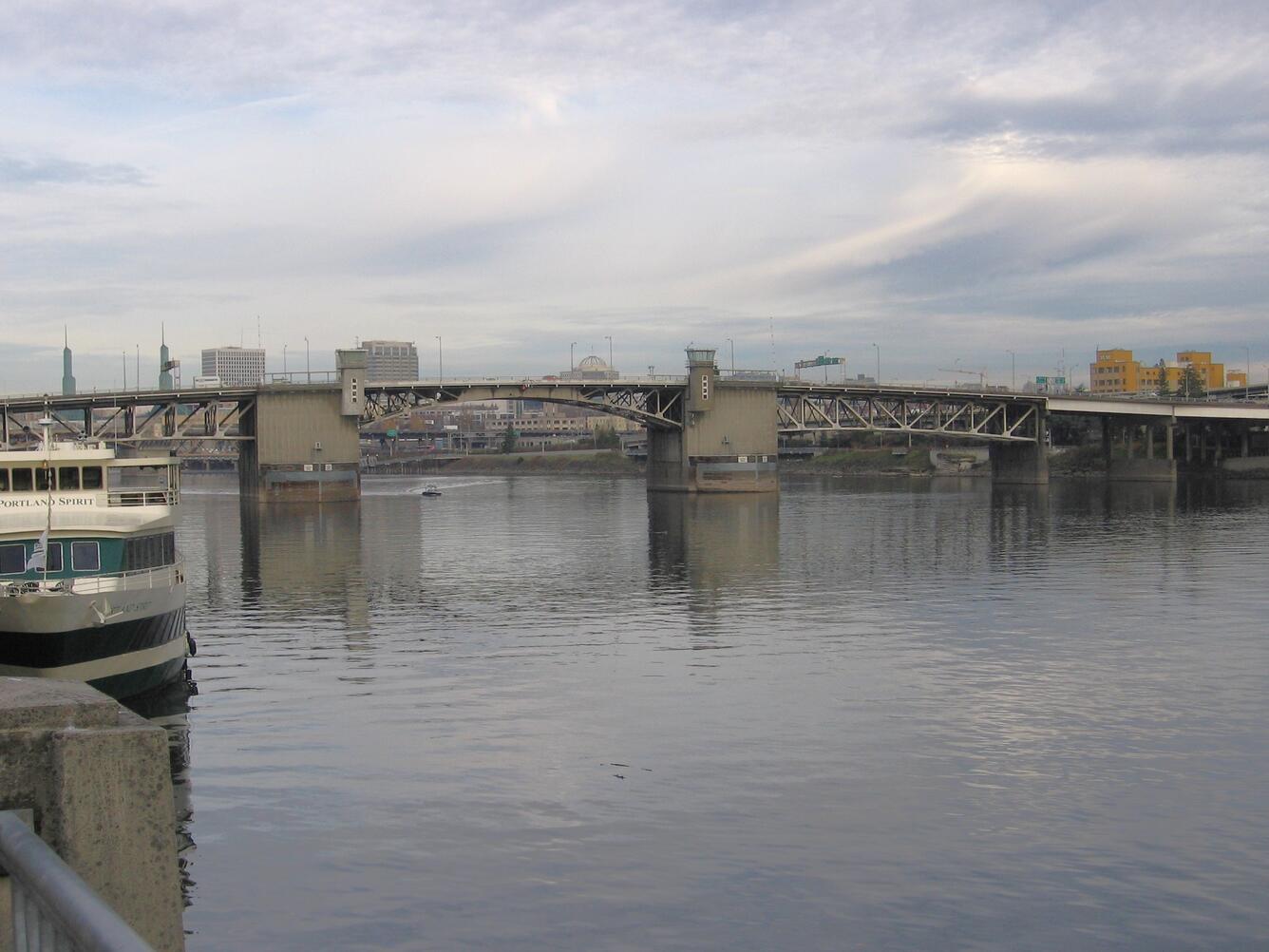 Metal and concrete bridge spans the river. Two concrete bridge piers are protected by wooden structures.