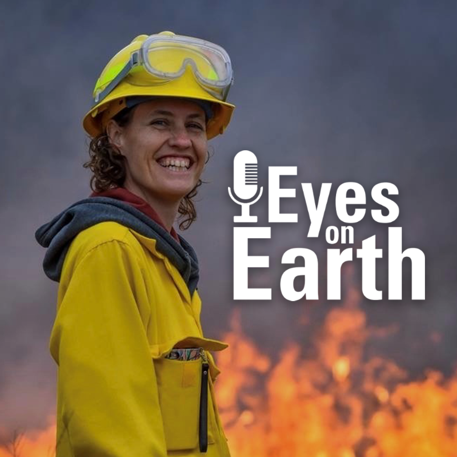 A woman smiles while dressed in a yellow suit with a fire burning in the background