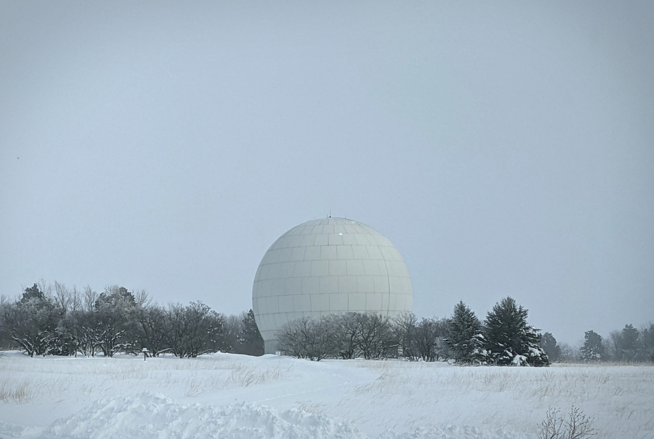 Snowy field with round white radome and dark line of trees in back