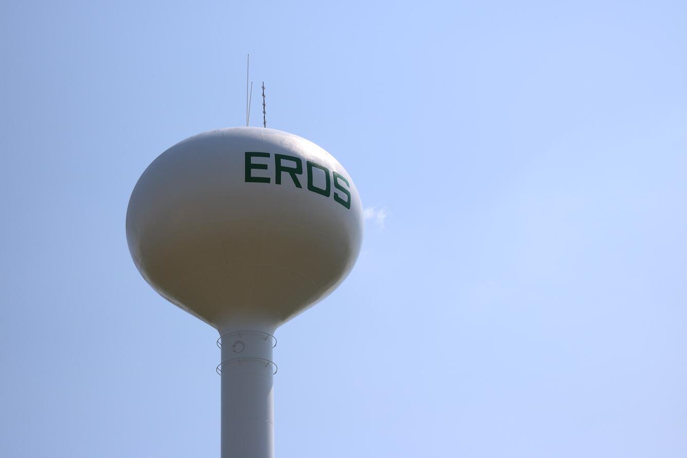 The round top of a white water tower with dark lettering appears against a clear blue sky 