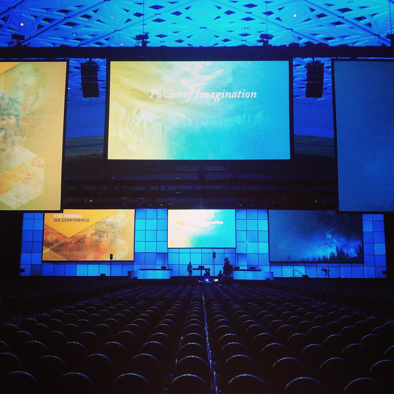 Backlit conference backdrop and stage and a row of seats in the foreground in a low-lit ballroom