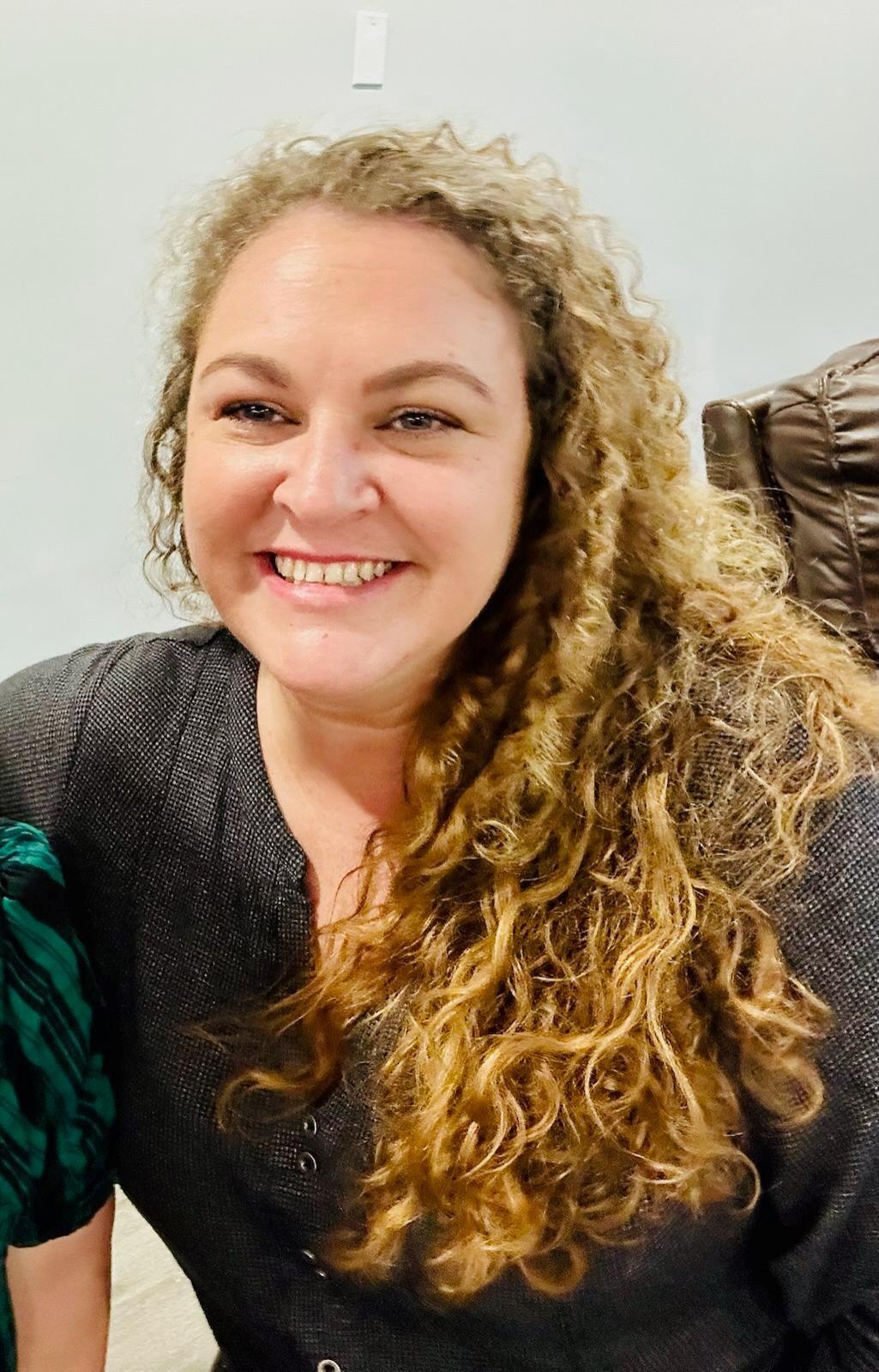 Headshot of a smiling woman with long, light brown curly hair.