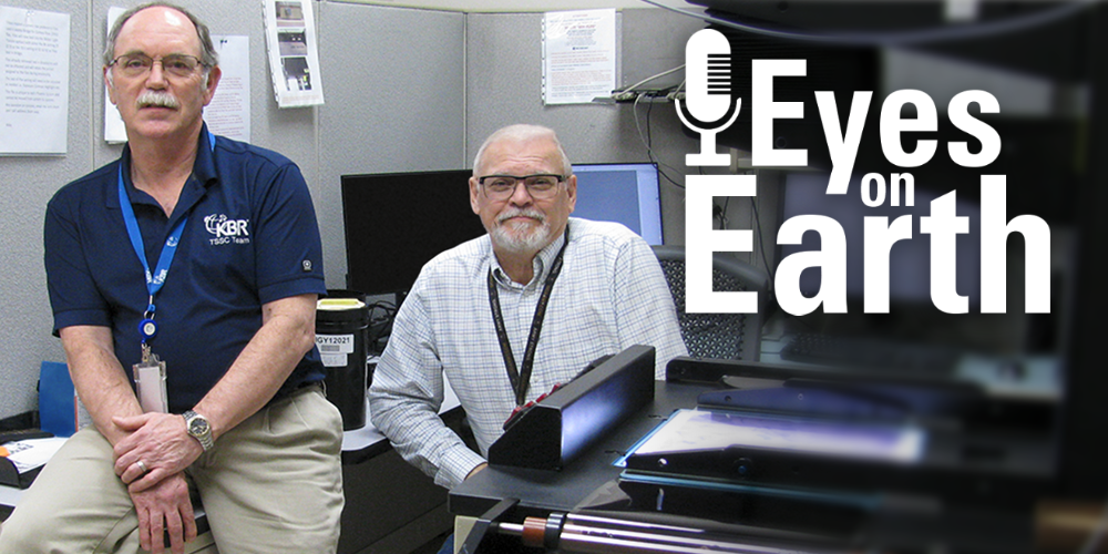 Two men seated in an office environment with a logo on the right
