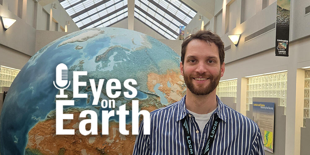 A man stands by a giant globe in a long hallway with skylights and a little white text on top