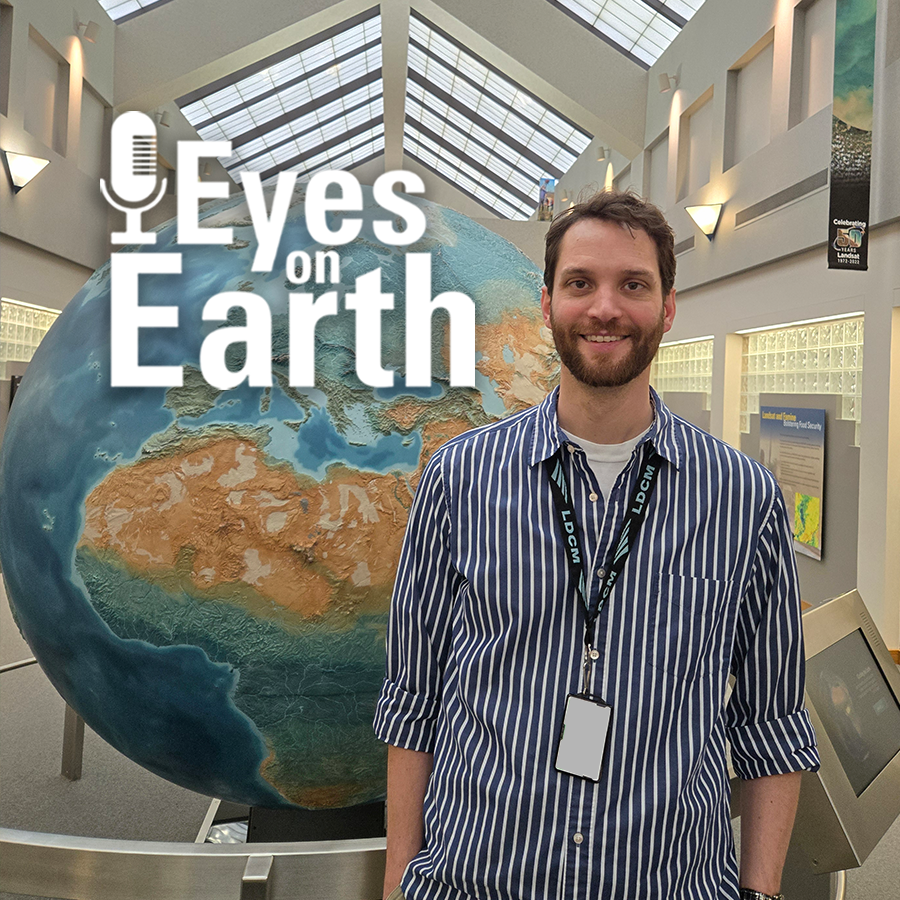 A man stands by a giant globe in a long hallway with skylights and a little white text on top