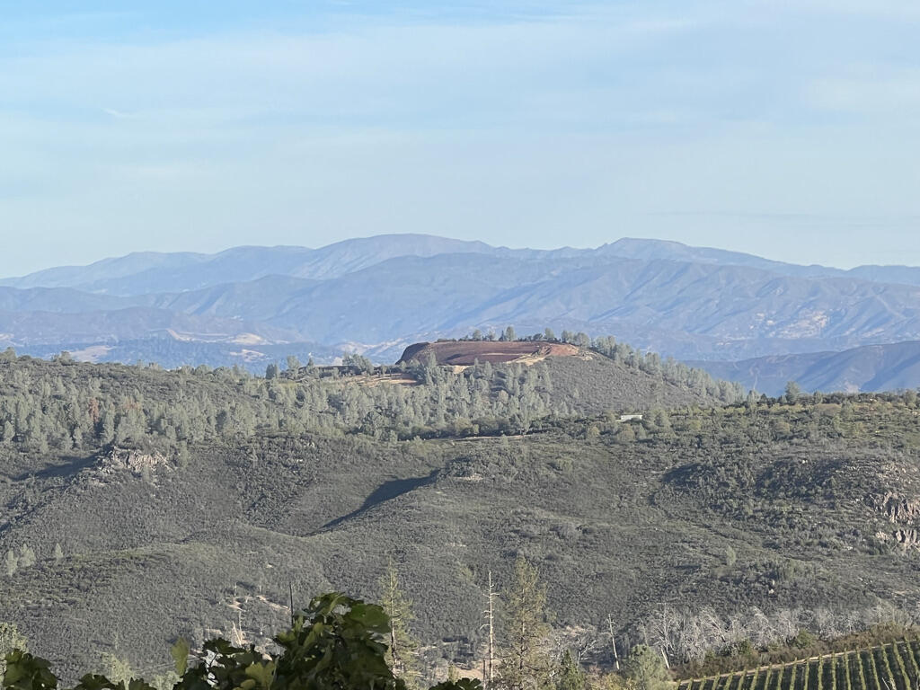 In the middle ground, a conical hill has been mined, revealing an orange interior. The flanks are lined with trees and brush.