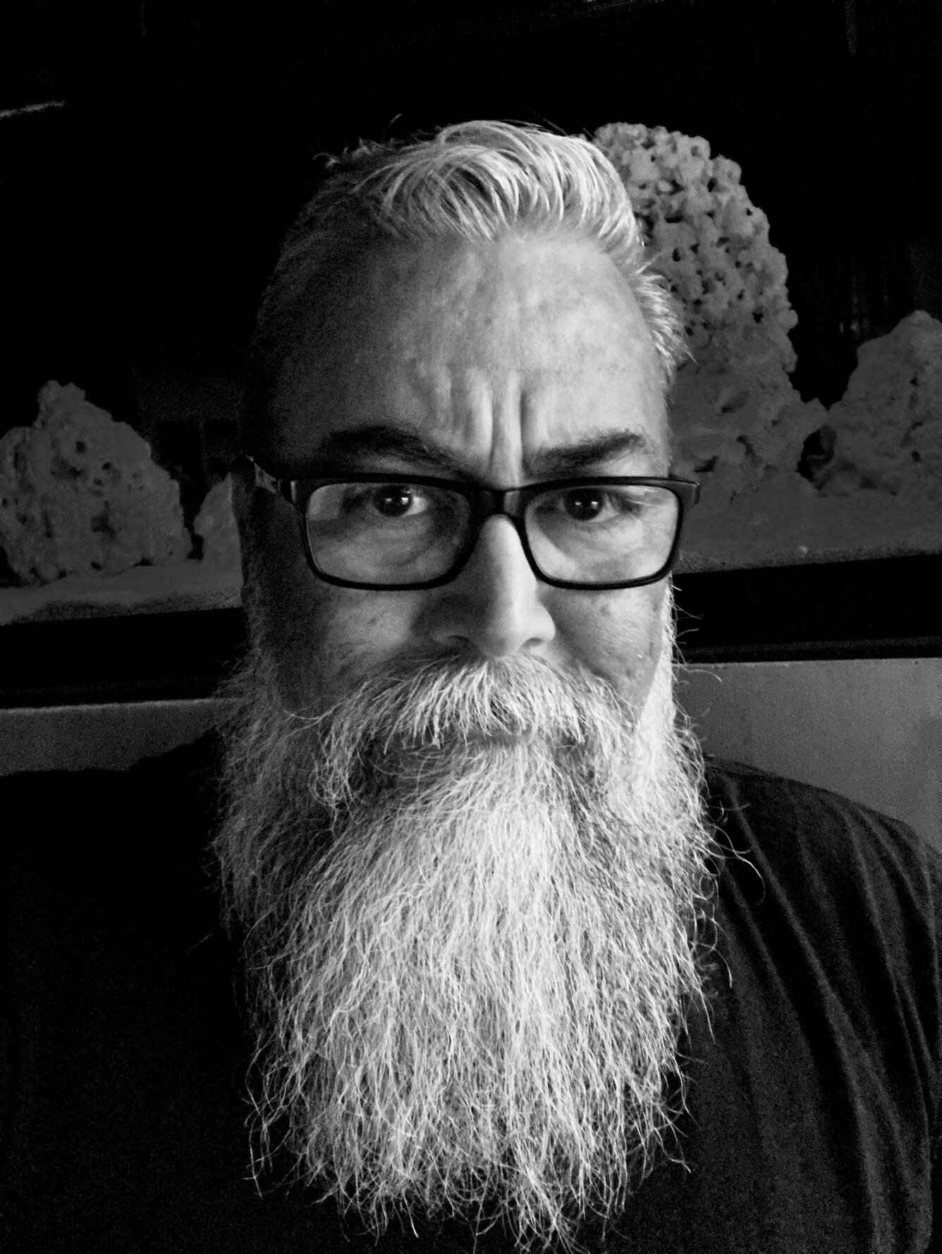 Black and white photo of biologist Ernie Valdez. Ernie is wearing dark-rimmed glasses and has a long beard. 