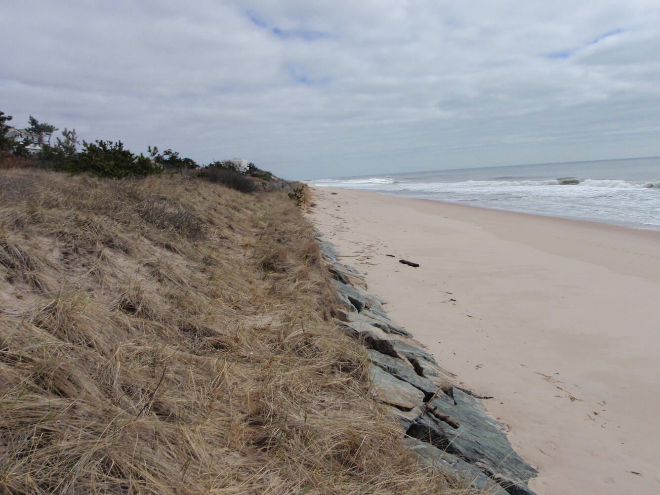 A human-made riprap rock seawall to protect an ocean dune at a beach is exposed by erosion