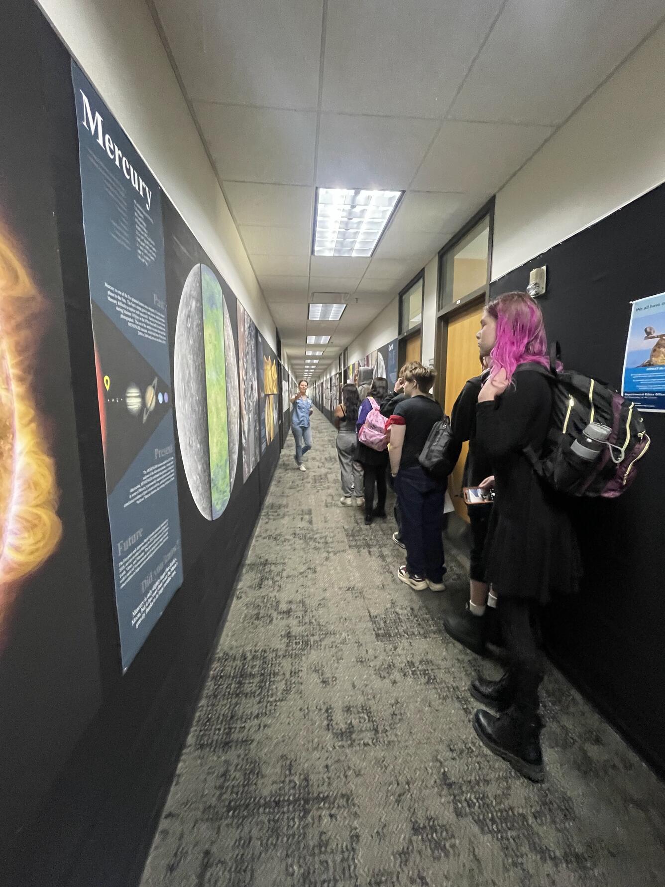 A USGS physical scientist speaks to students as they look at planetary posters in the Astrogeology building hallway 