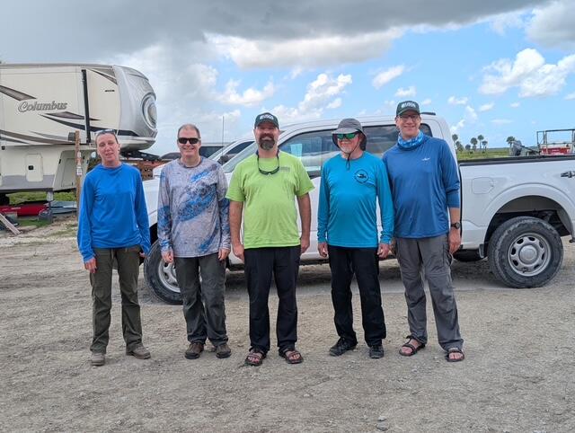 five people stand for a group shot in front of a truck
