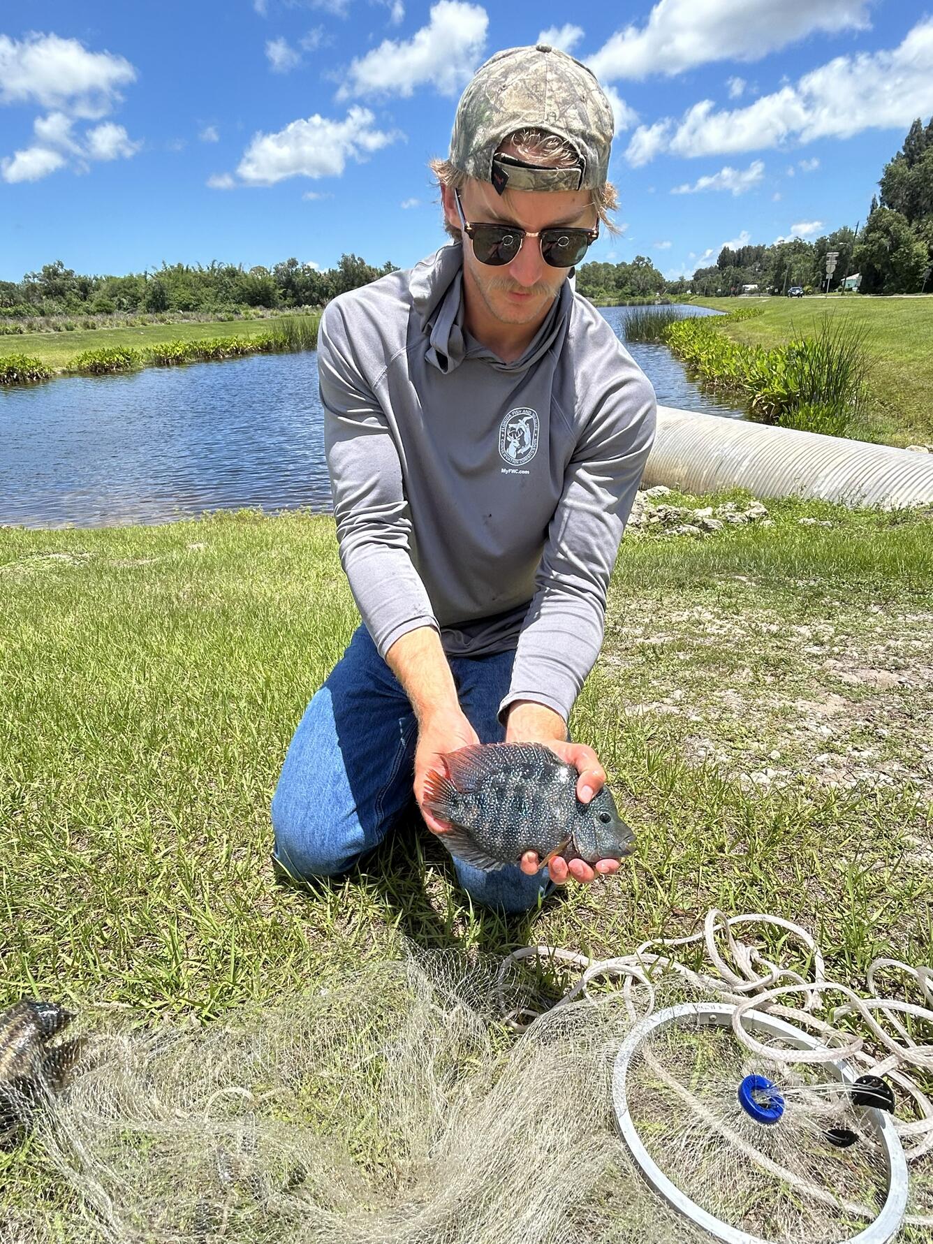 a man is shown holding a fish in front of a small body of water and a blue sky