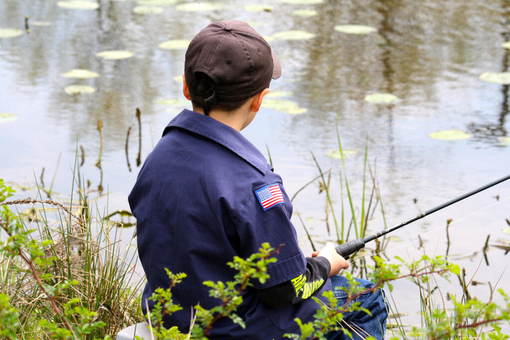 A boy sits fishing at a pond