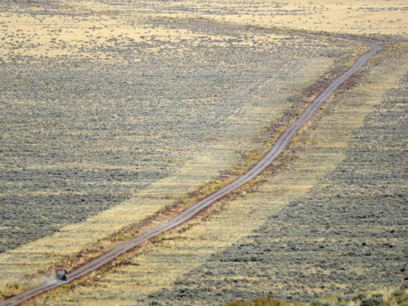 aerial view of a road, with mowed areas of sagebrush right next to the road and a Jeep driving