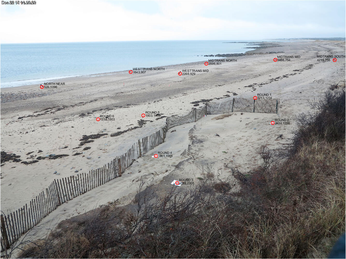 View looking along a beach with a fence and gentle water in background, and various spots on the photo are marked.